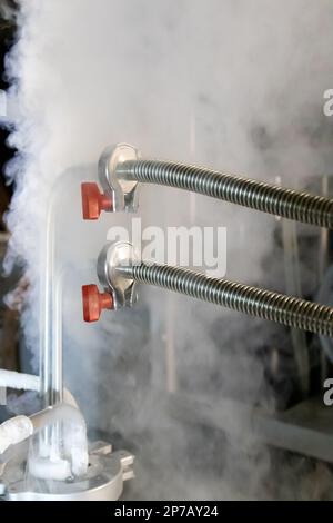 Flüssiges Stickstoffgas, das aus einem unter Druck stehenden Tank austritt und mit Metallrohren und roten Handventilen verbunden ist. Stockfoto