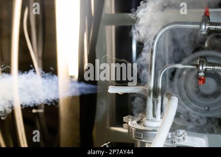 Flüssiges Stickstoffgas, das aus dem unter Druck stehenden Tank austritt, Thermogummischlauch, der mit Metallrohren und roten Handventilen verbunden ist. Stockfoto