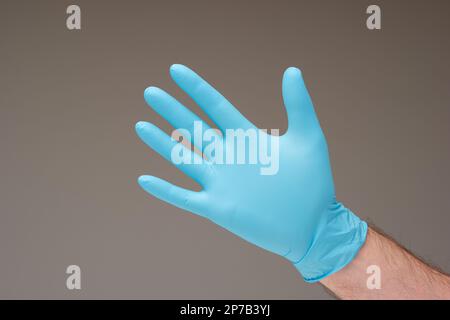 Blauer Einweghandschuh aus Latex, getragen von weißer männlicher Hand. Nahaufnahme des Studios, isoliert vor grauem Hintergrund. Stockfoto