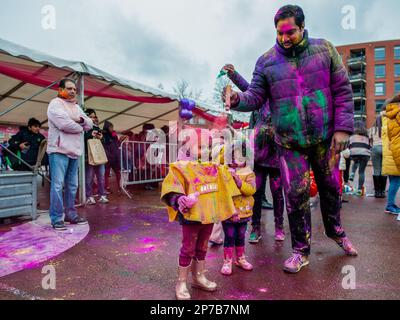 Den Haag. Niederlande, 07. 03. 2023, Ein Mann wirft während des Holi Festivals in Den Haag bunten Puder über seine beiden Kinder. Millionen Menschen auf der ganzen Welt feiern das jährliche Holi Hangámá Festival. In Den Haag, wo die größte indische Bevölkerung Europas zu finden ist, fand eine große Feier im multikulturellen transvaalen Viertel statt, wo die Teilnehmer bunt bunten Puder auf sich selbst und auf einander werfen. Diese Feier, auch bekannt als Fest der Farben, bedeutet die Feier der Ankunft des Frühlings, ein Neuanfang, und den Triumph des Göttlichen und des Guten. Stockfoto