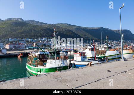 Fischerboote liegen im Hafen von Kalk Bay, Kapstadt, Westkap, Südafrika bei Sonnenuntergang vor Anker mit Blick auf die Häuser in Kalk Bay Stockfoto