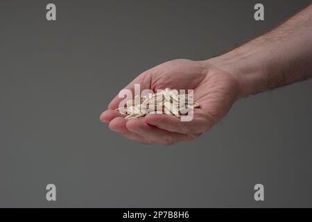 Ganze getrocknete Sonnenblumenkerne, die von männlichen weißen Händen gehalten werden. Draufsicht, Innenaufnahme, geringe Schärfentiefe. Stockfoto