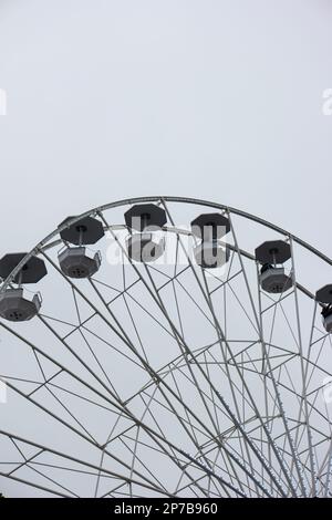 Leere Stühle am Riesenrad gegen den bewölkten Himmel. Nahaufnahme von Teleobjektiv, keine Leute. Stockfoto