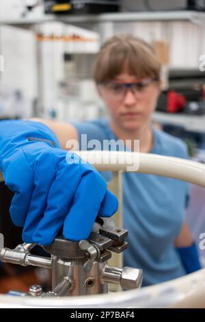 Wissenschaftlerin, die einen großen Flüssigstickstofftank mit ihrer Hand mit Schutzhandschuhen betreibt. Nahaufnahme, geringe Schärfentiefe, unscharf, unerkannt Stockfoto