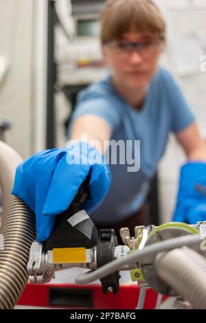Wissenschaftlerin, die einen großen Flüssigstickstofftank mit ihrer Hand mit Schutzhandschuhen betreibt. Nahaufnahme, geringe Schärfentiefe, unscharf, unerkannt Stockfoto