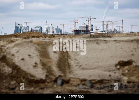 Hamburg, Deutschland. 08. März 2023. Die Silhouette von HafenCity mit der Konzerthalle Elbphilharmonie (l) und ihren zahlreichen Baustellen ist hinter der Sandfüllung zu sehen, um die Baustelle auf Grasbrook im Hafen vorzubereiten. Auf der jährlichen Pressekonferenz der HafenCity Hamburg GmbH wurden die Zukunftsstrategien in den Stadtentwicklungsgebieten Grasbrook, Science City Hamburg Bahrenfeld, Billebogen und HafenCity sowie weitere Themen vorgestellt. Kredit: Christian Charisius/dpa/Alamy Live News Stockfoto