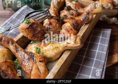 Gebratene Hähnchenschenkel in einer Holzschüssel auf rustikalem Hintergrund. Stockfoto