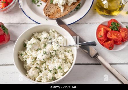 Marinierter Fetakäse oder Schafskäse mit Kräutern und Olivenöl, serviert als Salat mit gebratenem Brot auf einem weißen Tisch Stockfoto