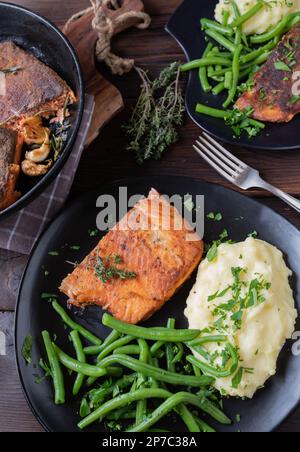 Gebratener Lachs mit Haut. Serviert mit Kartoffelpüree und grünen Bohnen auf einem dunklen Teller auf rustikalem Holztisch. Draufsicht Stockfoto