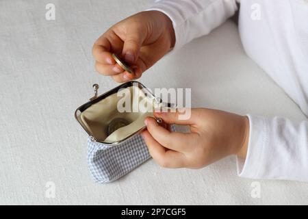 Kinderhände stecken Münzen in eine Brieftasche, Kleinkind mit Geld und Pusre in die Hände Stockfoto