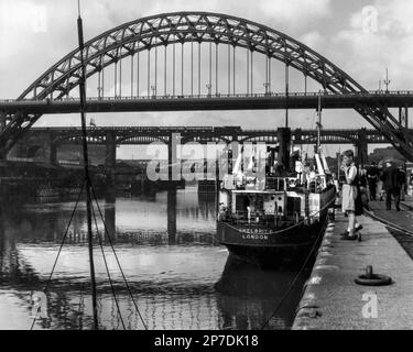 Steam Age Newcastle Upon Tyne, Tyne and Wear, England, Vereinigtes Königreich: Die Puffing-Lokomotive zieht Kutschen über die High Level Bridge jenseits der gewölbten Tyne Bridge und des Quayside der Stadt, wo Shelbrit 6, ein Shell-Mex- und BP-Küstentanker, vor Anker liegt. Das 797 Tonnen schwere dampfbetriebene Schiff wurde 1944 gebaut, transportierte Öl für Shell 1947-1964 und wurde 1973 in Palermo, Italien, verschrottet. Klassisches 1950-Schwarzweißfoto. Stockfoto