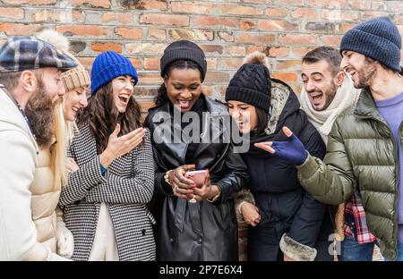 Multikulturelle urbane Freunde, die Spaß auf Mobiltelefonen haben, die warme Mode tragen – Frohe multikulturelle Freunde, die Zeit zusammen verbringen. Watchi Stockfoto