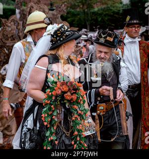 Eine Gruppe von Steampunken, die in einer Prozession entlang einer Straße laufen. Die Frau vorne trägt einen Kraken in einem Käfig. Stockfoto