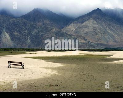 Friedlicher Blick auf eine Bank mit Blick auf die hohen Berge in der Wüste des Nubra-Tals, Ladakh, Indien Stockfoto