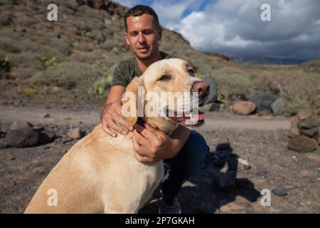 Ein labrador Retriever ist entspannt, während sein Besitzer ihn umarmt und das Halsband anlegt Stockfoto