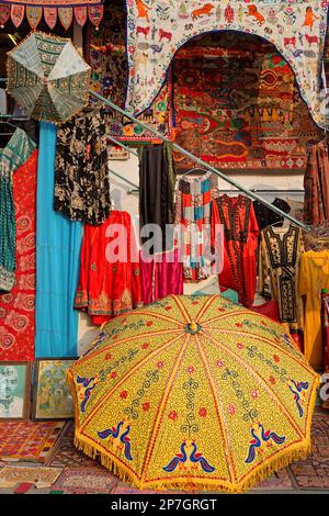 UDAIPUR, INDIEN, 5. November 2017 : Regenschirme, Teppiche und Schals, die in einem Straßenladen in Udaipur verkauft werden, bilden einen farbigen Rahmen. Stockfoto