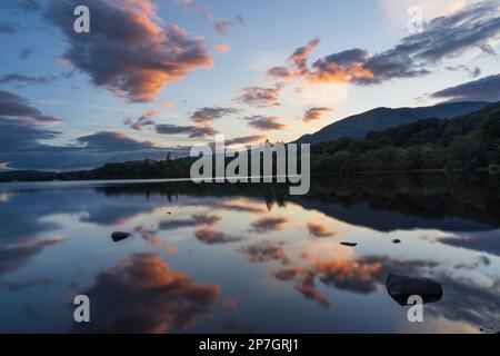 England, Cumbria, Lake District Nationalpark. Lakeland Hügel und ein farbenfroher Sonnenuntergang, der sich auf dem stillen Gesicht von Coniston Water reflektiert. Stockfoto