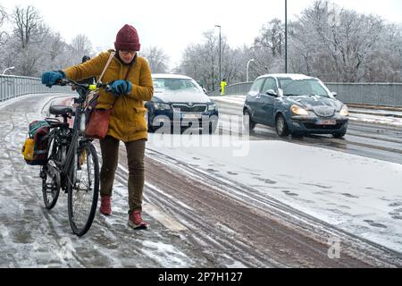 Radfahrer läuft zu Fuß und hält Fahrrad auf rutschigem Radweg/Radweg bedeckt mit Graupel während unerwarteter später Schneeschauer im März, Gent, Belgien Stockfoto