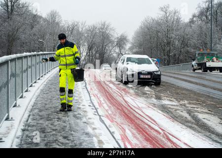 Stadtarbeiter, der Salz auf rutschigem Pflaster auf einer mit Graupel bedeckten Brücke während des unerwarteten späten Schneeschauers im März 2023 in Gent, Belgien, ausstreut Stockfoto