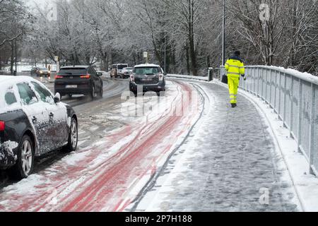 Stadtarbeiter, der Salz auf rutschigem Pflaster auf einer mit Graupel bedeckten Brücke während des unerwarteten späten Schneeschauers im März 2023 in Gent, Belgien, ausstreut Stockfoto