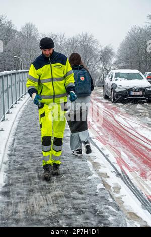 Stadtarbeiter, der Salz auf rutschigem Pflaster auf einer mit Graupel bedeckten Brücke während des unerwarteten späten Schneeschauers im März 2023 in Gent, Belgien, ausstreut Stockfoto