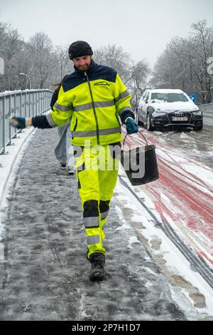 Stadtarbeiter, der Salz auf rutschigem Pflaster auf einer mit Graupel bedeckten Brücke während des unerwarteten späten Schneeschauers im März 2023 in Gent, Belgien, ausstreut Stockfoto