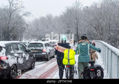 Radfahrer laufen zu Fuß und halten Fahrräder auf rutschigem Pflaster / mit Schneeregen bedeckter Fußweg während unerwarteter später Schneeschauer im März, Gent, Belgien Stockfoto