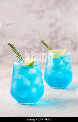 Erfrischendes blaues Getränk oder Cocktail mit Eis, garniert mit einer Scheibe Limette und Rosmarin. Stockfoto