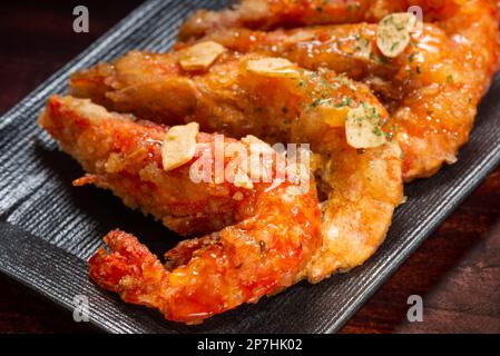 Gegrillte Garnelen in Teig mit Knoblauch in süßer und saurer Sauce auf schwarzem japanischem Teller. Stockfoto