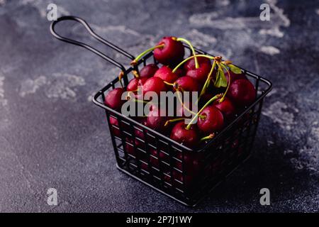 Frische süße rote Kirschen im Korb auf dunklem Hintergrund, selektiver Fokus Stockfoto