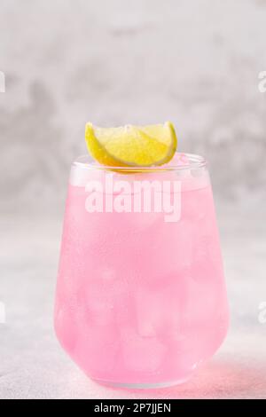 Erfrischendes rosa Getränk oder Cocktail mit Eis, garniert mit einem Stück Limette. Stockfoto