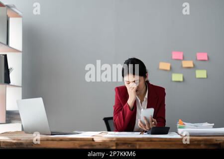 Gestresste und ernsthafte junge asiatische Geschäftsfrau mit ihrem Smartphone, die Probleme mit ihrem Handy hat Stockfoto