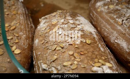 Brotlaibe von Roggenbrot liegen auf dem Holzbakerregal. Nahaufnahme. Einkaufen im Supermarkt. Konzept des Verkaufs von Lebensmitteln Stockfoto