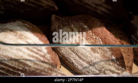 Brotlaibe von Roggenbrot liegen auf dem Holzbakerregal. Nahaufnahme. Einkaufen im Supermarkt. Konzept des Verkaufs von Lebensmitteln Stockfoto
