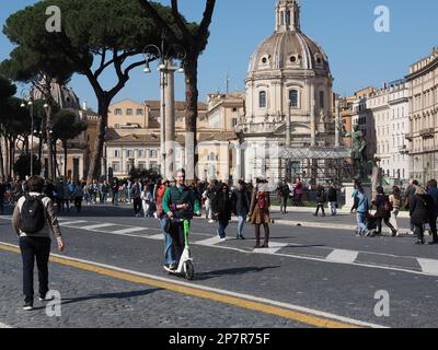 Junges Paar, das einen gemieteten elektrischen Roller auf der Via Dei Fori Imperiali in Rom, Italien, benutzt Stockfoto