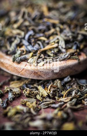 Getrocknete Teeblätter werden in heißes Wasser für ein entspannendes Getränk gegeben. Zutat auf Holzlöffel. Stockfoto