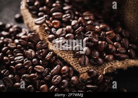 Ein Haufen dunkelbrauner gerösteter Kaffeebohnen in einem Leinensack, bereit zum Mahlen zu Pulver. Stillleben. Stockfoto