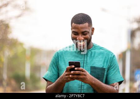 Young African man Mobile-Banking unterwegs mit Smartphone, Porträt eines ghanaischen Mannes mit Handy Stockfoto
