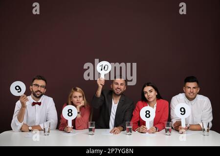 Jury mit unterschiedlichen Punktezeichen am Tisch auf braunem Hintergrund Stockfoto