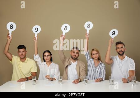 Jury mit unterschiedlichen Punktezeichen am Tisch auf beigefarbenem Hintergrund Stockfoto