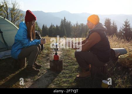 Ein junges Paar trinkt Kaffee in der Nähe von Campingzelten in den Bergen Stockfoto