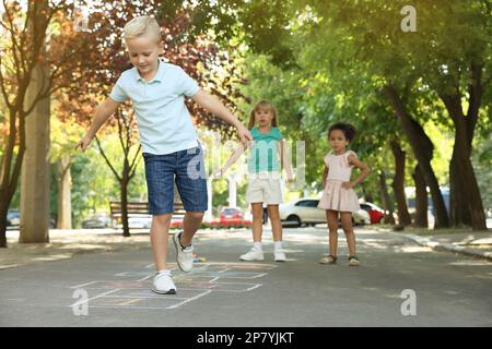 Kleine Kinder, die im Freien mit Kreide auf Asphalt gezeichnet Hopscotch spielen Stockfoto