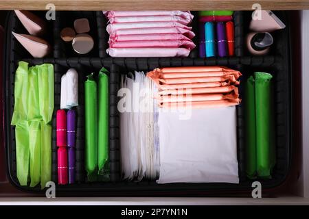 Offene Schublade mit Menstruationseinlagen, Tampons, Make-up- und Hautpflegeprodukten, Draufsicht Stockfoto