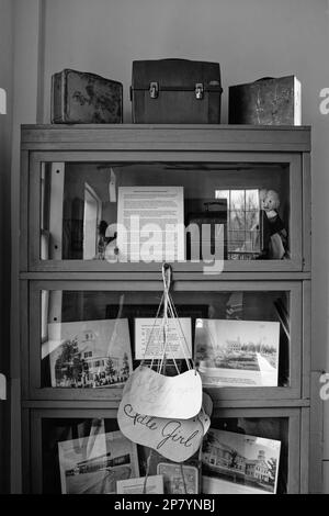 Ein Kuriositätenschrank mit Glastüren, in dem klassische Lunchboxen, Puppen und Fotos im Hauptgebäude des Tuck Museum of Hampton History ausgestellt sind Stockfoto