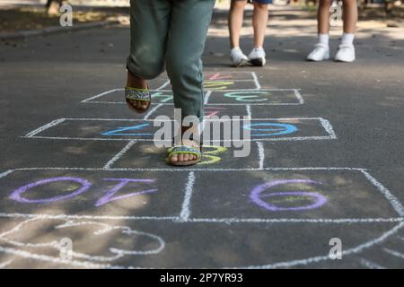 Ein kleines afroamerikanisches Mädchen, das Hopscotch spielt, gemalt mit Kreide auf Asphalt draußen, Nahaufnahme. Glückliche Kindheit Stockfoto