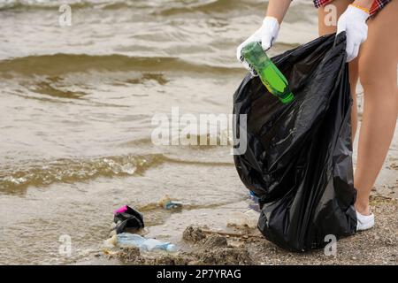 Frau in Handschuhen mit Müllsack, Müll am Strand einsammeln, schließen Stockfoto