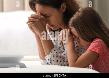 Reife Frau mit ihrer kleinen Enkelin betet zusammen für die Bibel im Schlafzimmer Stockfoto