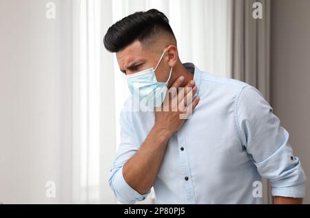 Der Mann in der medizinischen Maske leidet unter Schmerzen beim Atmen in Innenräumen Stockfoto
