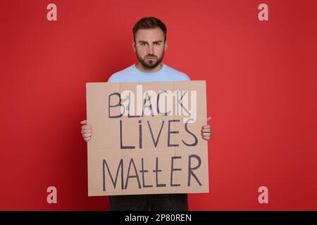 Junger Mann mit einem Schild mit der Phrase "Schwarze Leben sind wichtig" auf rotem Hintergrund. Beenden Sie den Rassismus Stockfoto