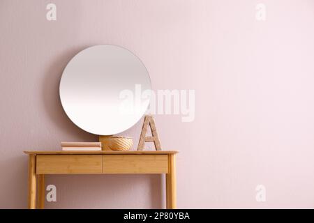 Bücher und Dekoration auf einem Konsolentisch nahe beigefarbener Wand mit Innenspiegel, Platz für Text. Innendesign Stockfoto